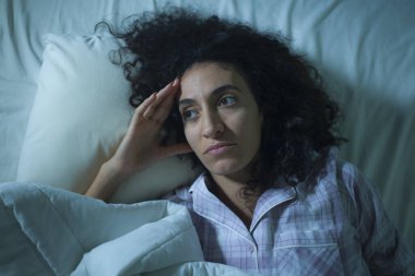 Genç üzgün ve bunalımlı kıvırcık saçlı, yatakta uykusuz, düşünceli, depresyon sorunu ve uykusuzluk sorunu yaşayan bir kadın.