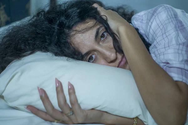 Νεαρή λυπημένη και καταθλιπτική ισπανόφωνη γυναίκα με σγουρά μαλλιά άγρυπνη στο κρεβάτι ξύπνια και στοχαστικό αίσθημα ανησυχίας που υποφέρει από κατάθλιψη και διαταραχή αϋπνίας — Φωτογραφία Αρχείου