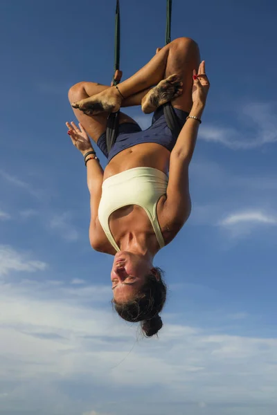 aerial yoga meditation workout  isolated on blue sky - young attractive and healthy woman practicing aero-yoga training balance body and mind control hanging from ropes