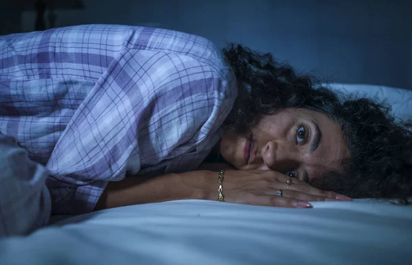 Dramatic night lifestyle portrait of young sad and depressed middle eastern woman with curly hair sleepless in bed awake and thoughtful feeling worried suffering depression — Stock Photo, Image