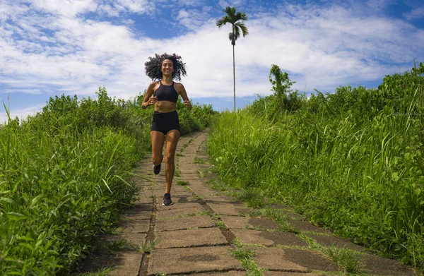 happy female runner training on countryside road - young attractive and fit jogger woman doing running workout outdoors at beautiful track in healthy lifestyle and sport