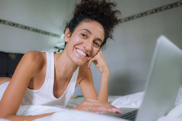 Домашний образ жизни портрет молодой счастливой и привлекательной хипстерской женщины, лежащей уютно на кровати, расслабляясь на ноутбуке или наслаждаясь Интернетом социальные медиа улыбаясь весело — стоковое фото