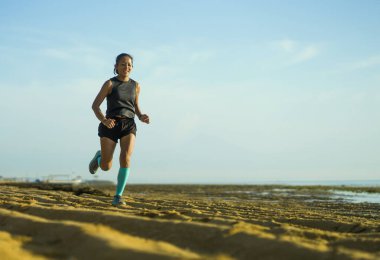 Genç ve mutlu Endonezyalı kadın kompresyon çorapları içinde sahilde neşeli koşu yaparken spor yaparken çekilmiş. 