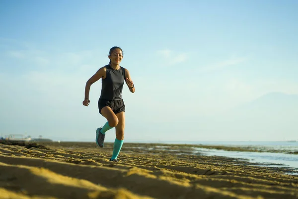 На відкритому повітрі портрет молодої привабливої і щасливої індонезійської жінки в стиснених шкарпетках біжить весело на пляжі, роблячи тренування — стокове фото