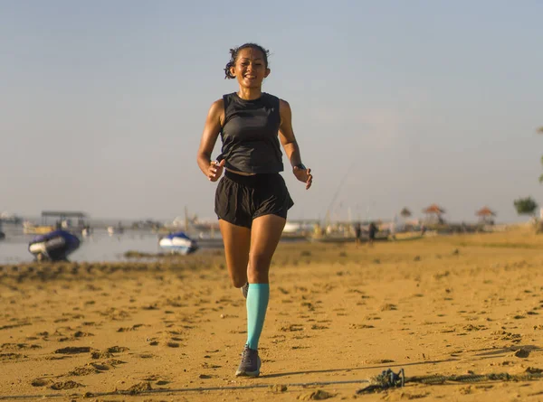 Genç ve mutlu Endonezyalı kadın kompresyon çorapları içinde sahilde neşeli koşu yaparken spor yaparken çekilmiş. — Stok fotoğraf