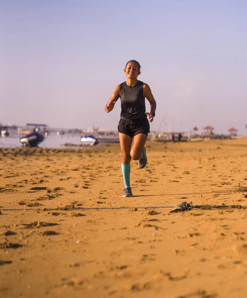 Genç ve mutlu Endonezyalı kadın kompresyon çorapları içinde sahilde neşeli koşu yaparken spor yaparken çekilmiş. — Stok fotoğraf