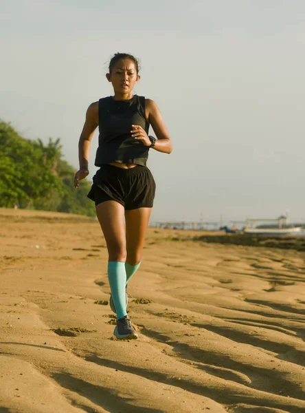 На відкритому повітрі портрет молодої привабливої і атлетичної індонезійської жінки в стиснених шкарпетках біжить по пляжу, роблячи важке тренування — стокове фото