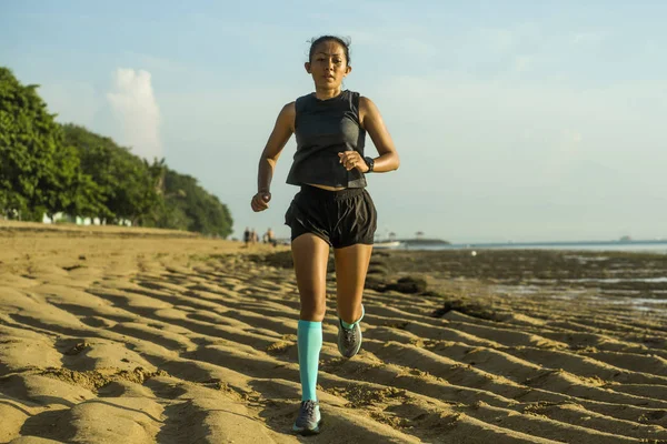 Outdoors fitness portrait of young attractive and athletic Asian Indonesian woman in compression socks jogging on the beach doing running workout training hard — Stockfoto