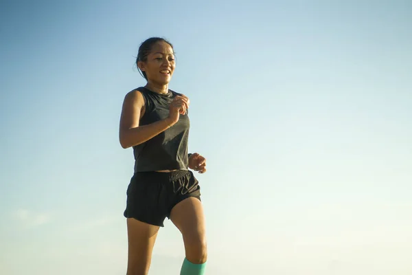 Портрет молодої привабливої і спортивної індонезійської жінки, якій за 40 років, що біжить на синьому тлі неба, посміхається, коли вона важко тренується. — стокове фото