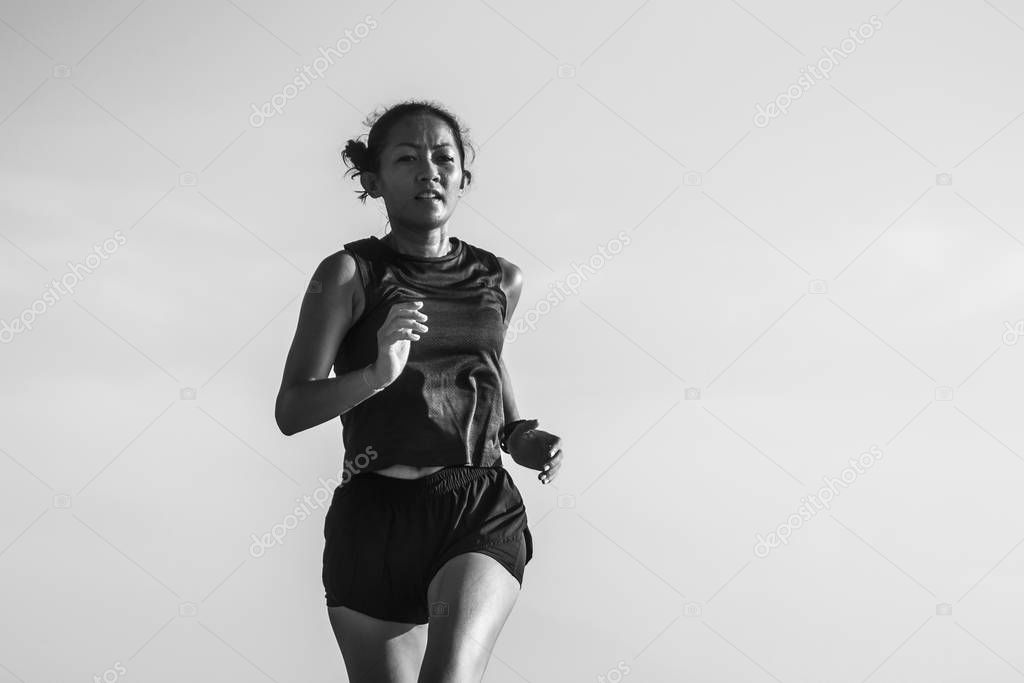 outdoors fitness portrait of young attractive and athletic Asian Indonesian woman in her 40s running on blue sky background doing intervals workout in athlete training