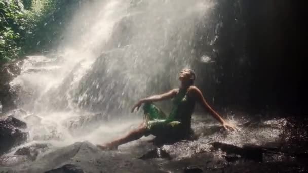 バリの滝の美しさに圧倒されたサロンの若い魅力的なアジア系インドネシア人女性熱帯ジャングルは 水が彼女の気持ちに自由で至福を与えます — ストック動画