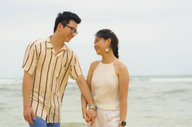 Genç mutlu Asyalı Çinli çiftin romantik ve tatlı bir portresi. Güzel bir sahilde tatilin tadını çıkarıyorlar. Deniz kenarında birlikte yürüyorlar.