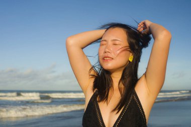 Çekici ve mutlu Asyalı bir kadının doğal yaşam tarzı portresi. Mayo giymiş güzel bir plaj cennetinde yürüyor. Rahatlamış ve keyifli tatillerin tadını çıkarıyor. 