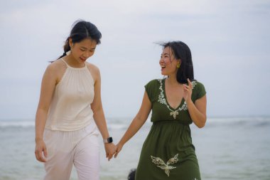 Genç, güzel ve mutlu bir çift çekici Asyalı kadın sahilde birlikte yürüyor tatilin tadını çıkarıyor kız arkadaşlığı kavramında özgür ve neşeli hissediyorlar.