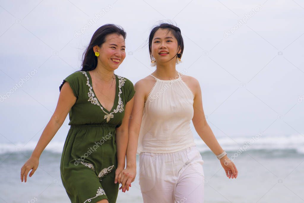 young beautiful and happy couple of attractive Asian Chinese women walking together relaxed at the beach enjoying holidays in gay lesbian love or close girlfriends relationship concept
