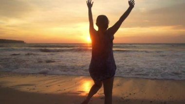 Genç mutlu ve heyecanlı Asyalı kadının silueti güzel sahilde tatil gezisi konseptiyle Bali adasının tropikal sahillerinde altın saatin tadını çıkarıyor.