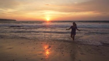 Genç mutlu ve heyecanlı Asyalı kadının silueti güzel sahilde tatil gezisi konseptiyle Bali adasının tropikal sahillerinde altın saatin tadını çıkarıyor.