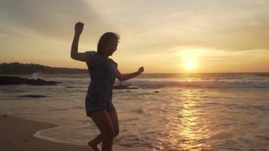 Genç mutlu ve heyecanlı Asyalı kadının silueti güzel sahilde tatil gezisi konseptiyle Bali adasının tropikal sahillerinde altın saatin tadını çıkarıyor.