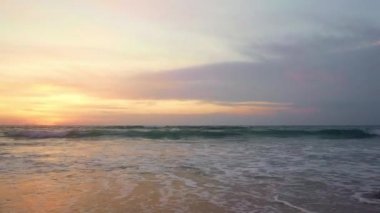 Gün batımında, turuncu gökyüzünün altında sörf yapan sörfçülerin isimsiz siluetleriyle yaz tatillerinde ve seyahat konseptinde tropik cennet manzarasının güzel bir manzarası.