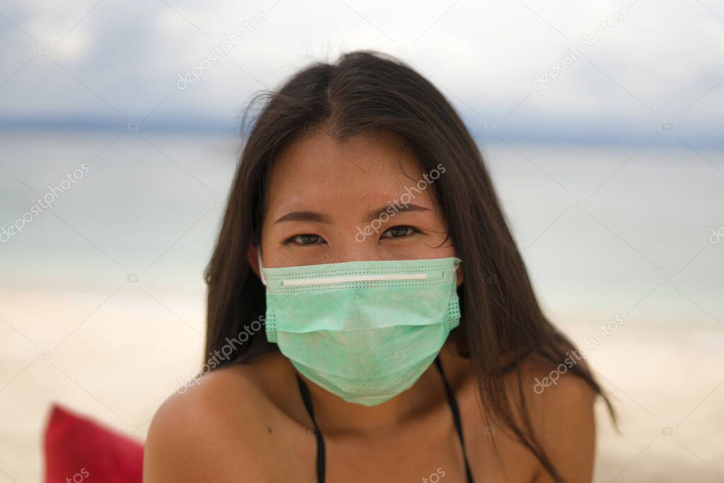 use of medical face mask in public places- young attractive Asian Chinese woman enjoying beach holidays wearing bikini and protective facial mask in prevention vs virus infection 