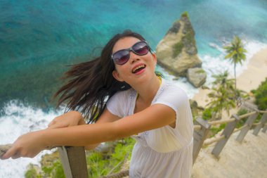 Güneş gözlüklü güzel ve mutlu bir Asyalı kadın yaz tatillerinde elmas şekilli kaya kayalıklarıyla tropik cennet sahillerinde denizin tadını çıkarıyor.