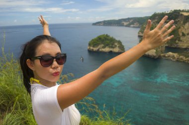 Güneş gözlüklü, güzel ve mutlu Asyalı kadın yaz tatillerinde elmas kayalıklı tropik cennet sahili manzarasından inanılmaz bir sahnenin keyfini çıkarıyor. 