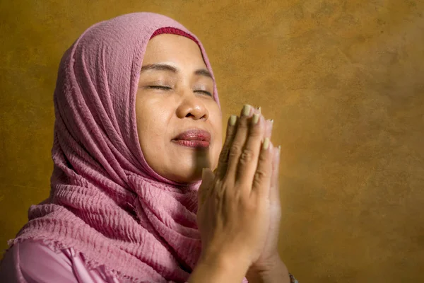 isolated studio portrait of happy and positive senior muslim woman in her 50s wearing traditional Islam hijab head scarf praying in Islamic culture and religion concept