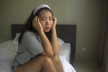 Genç, üzgün ve depresif bir Asyalı kadın. Saç bandı takmış, ev kıyafetleri giymiş. Düşünceli, düşünceli ve virüs salgınından korkan bir kadın. 