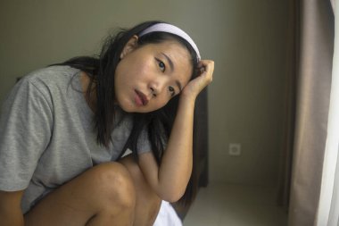 Genç, üzgün ve depresif bir Asyalı kadın. Saç bandı takmış, ev kıyafetleri giymiş. Düşünceli, düşünceli ve virüs salgınından korkan bir kadın. 