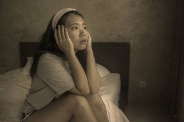 Genç, üzgün ve üzgün Asyalı bir kız. Saç bandında evde oturuyor. Düşünceli ve endişeli. 