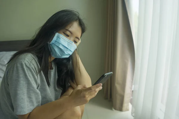 パンデミックウイルス発生 若い美しい恐怖と心配医療マスクのアジアの中国人女性隔離対Covid 19感染症で自宅で携帯電話のロックダウンとオンラインニュースをチェック — ストック写真