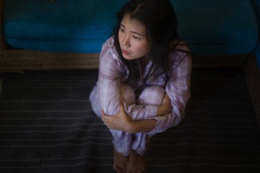 Evinde pijamalı, üzgün, üzgün, Asya 'lı genç bir kadının dramatik siyah portresi oturma odasındaki kanepede oturuyor mutsuz ve kalbi kırık bir şekilde acı çekiyor.