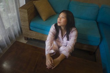 Evinde pijamalarıyla oturan üzgün ve üzgün Asyalı genç bir kadının dramatik karanlık portresi. Oturma odasındaki kanepede oturuyor. Mutsuz ve kafası karışık, kırık kalp ağrısı çekiyor.