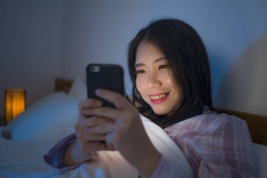 Genç, güzel, mutlu ve rahat Asyalı bir kadının portresi yatakta cep telefonuyla oynayan internet ve sosyal medya bağımlılığı ve aşırı kullanımı.