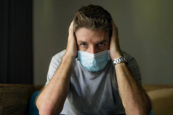 covid-19 virus lockdown - sad and worried man on his 30s or 40s covered with medical mask thinking and feeling scared in quarantine following stay at home instructions to contain virus pandemic