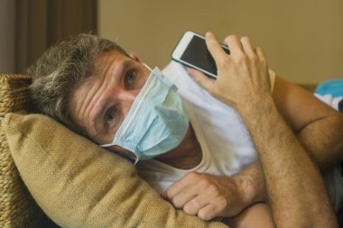 Covid-19 virüs salgınıyla ilgili internetten gelen haberlere göre yüz maskeli bir adam ev karantinasında. Bulaşıcı hastalık hakkında internet bilgilerini kontrol ediyor. Korkmuş ve endişeli.