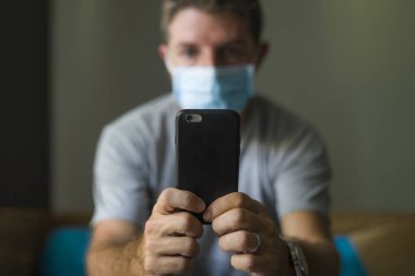 Covid-19 virüs salgınıyla ilgili internetten gelen haberlere göre yüz maskeli bir adam ev karantinasında. Bulaşıcı hastalık hakkında internet bilgilerini kontrol ediyor. Korkmuş ve endişeli.