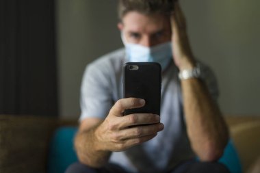 Covid-19 virüs salgınıyla ilgili internetten gelen haberlere göre yüz maskeli bir adam ev karantinasında. Bulaşıcı hastalık hakkında internet bilgilerini kontrol ediyor. Korkmuş ve endişeli.