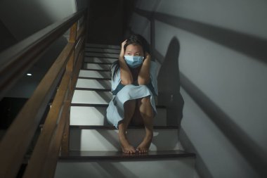 Korkak ve endişeli Koreli Koreli bir kadının hüzünlü portresi. Ev kilitlenmesi ve karantina sırasında dramatik bir ışık altında virüsler salgını sırasında merdivenlerde oturuyor.