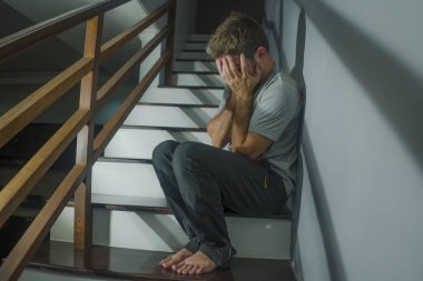 Depresyonda olan üzgün ve çaresiz bir adamın korku filmi portresi ya da evdeki merdivenlerde oturan umutsuz, çaresiz ve bunalmış bir adamın portresi.