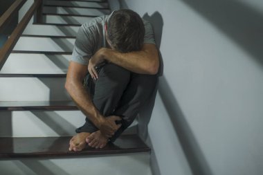 Depresyonda olan üzgün ve çaresiz bir adamın korku filmi portresi ya da evdeki merdivenlerde oturan umutsuz, çaresiz ve bunalmış bir adamın portresi.
