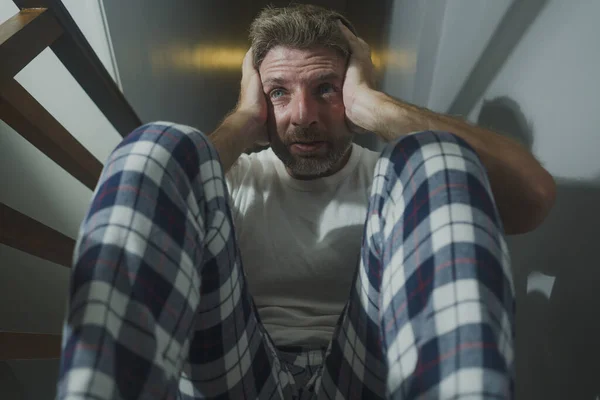 horror movie style portrait of sad and desperate man in pajamas suffering depression problem or mental disorder sitting on staircase at home hopeless crying overwhelmed and helpless