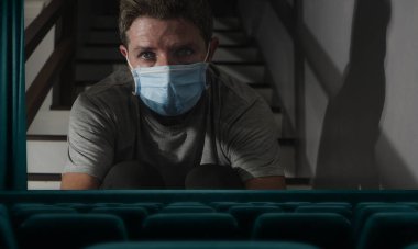 2020 COVID-19 virüslü boş sinema projeksiyonunun kavramsal kurgu görüntüsü koruyucu maskeli adamı karantina evindeki kilit altında gösteriyor.