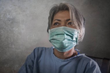 Covid-19 virüsü hastalık yayıyor. Koronavirüs enfeksiyonu kapmış, hasta önlüklü ve maskeli, korkmuş ve üzgün olgun bir kadın. İyileşme umudu içinde.
