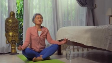 Ev hayatı. 50 'li yaşlarında güzel ve mutlu olgun bir kadın. Asya deco yatak odasında yoga yapıyor ve meditasyon yapıyor.