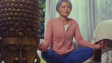 Ev hayatı. 50 'li yaşlarında güzel ve mutlu olgun bir kadın. Asya deco yatak odasında yoga yapıyor ve meditasyon yapıyor.