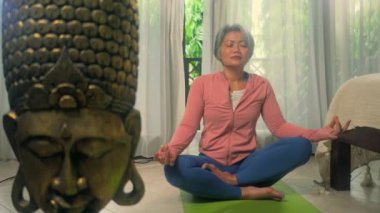 Ev hayatı. 50 'li yaşlarında güzel ve mutlu olgun bir kadın. Asya deco yatak odasında yoga yapıyor ve meditasyon yapıyor.