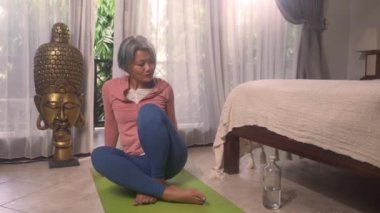 Ev hayatı tarzı. 50 'li yaşlarında güzel ve mutlu, olgun bir kadın. Asya deco yatak odasında spor yaptıktan sonra gülümsüyor ve sağlıklı yaşlanma konseptiyle yoga yapıyor.