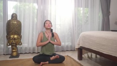 Genç, güzel ve mutlu Asyalı kadın evinde yoga yapıyor. Vücut ve zihin rahatlığı ve meditasyon egzersizleri yapıyor. Mutluluk konseptinde kendini neşeli ve pozitif hissediyor.