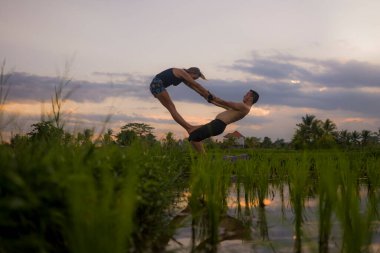 Açık havada günbatımı akroyogası silueti. Genç mutlu ve zinde çift güzel pirinç tarlasında akro yoga talimi yapıyor. Doğanın ve sağlıklı yaşam tarzının tadını çıkarıyor. 